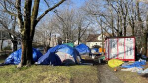 Tents at a park in Halifax are covered in tarps. The park is small, and some tents are collapsed. Garbage and tarps are strewn on the ground.